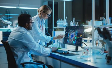 Female Research Scientist With Bioengineer Working On A Personal Computer With Screen Showing Virus Analysis Software User Interface. Scientists Developing Vaccine, Drugs And Antibiotics In Laboratory